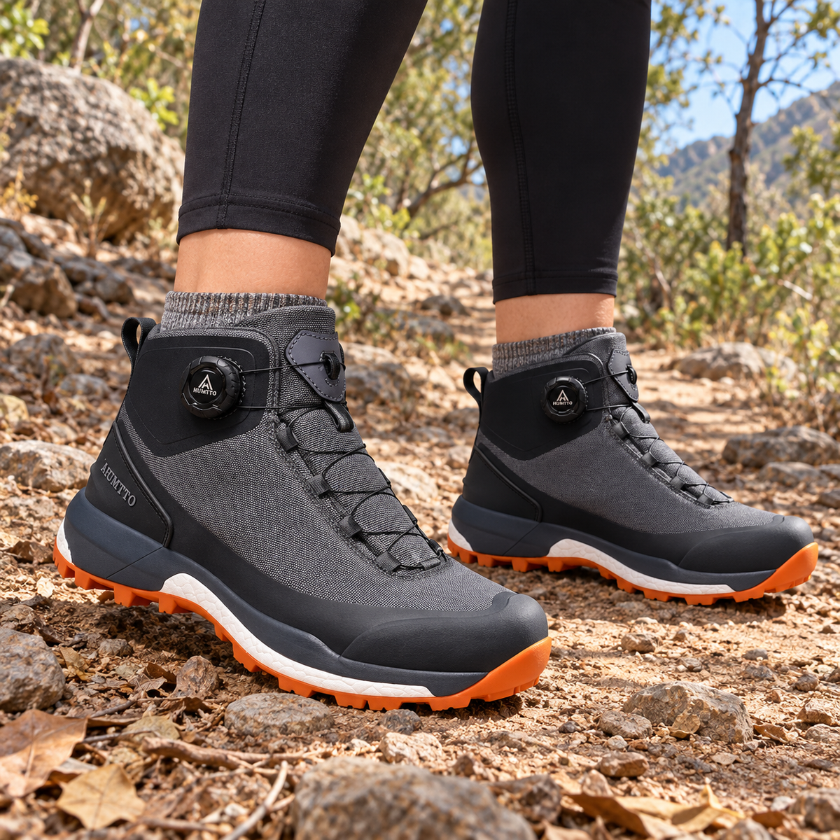 Paire de chaussures de randonnée femme orthopédiques gris foncé et orange portée sur sentier